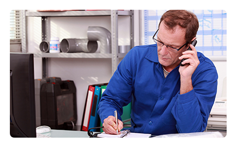 Man Sitting at Desk Writing in Notebook and Talking on Cell Phone.